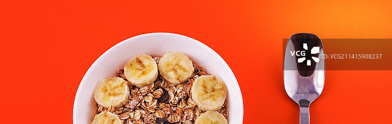 橙色背景上的燕麦粥、香蕉片和勺子，健康食品概念图片素材