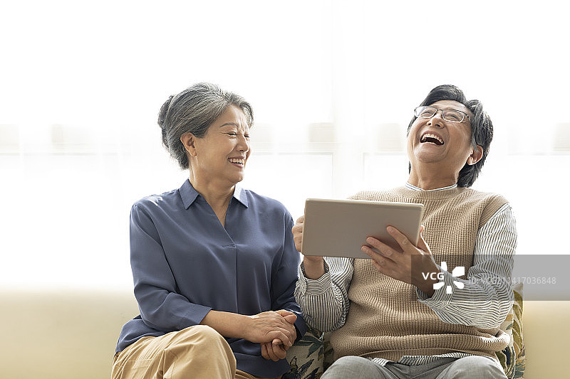 快乐的老年夫妇在客厅使用平板电脑图片素材