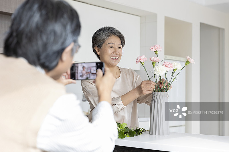 老年男子在家用手机给插花的妻子拍照图片素材