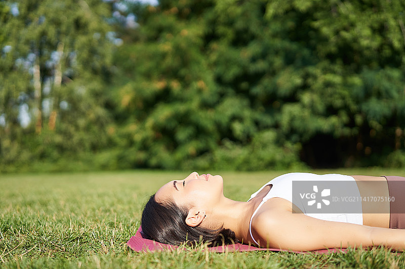 年轻的健身女孩躺在草坪上的运动垫上，呼吸图片素材