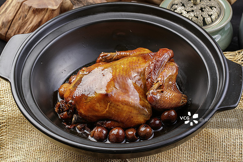 黑色砂锅装的板栗鸡摆放在麻布垫子上图片素材