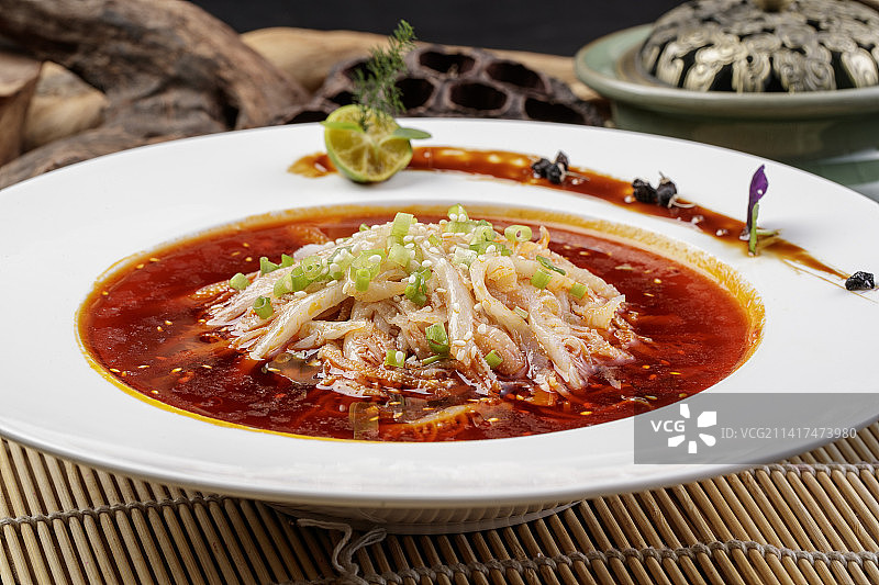 圆形瓷盘装的红油肚丝摆放在寿司帘上图片素材