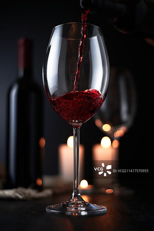 将红酒倒入酒杯，深色背景上的静物图片素材