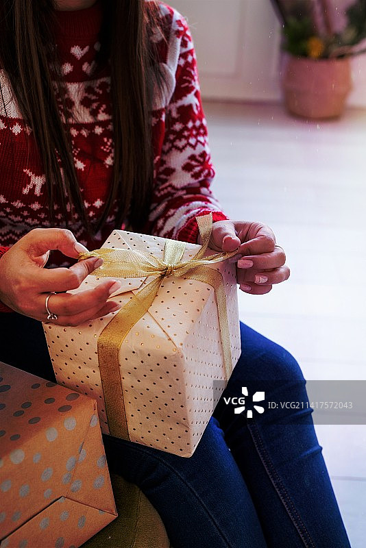 坐在沙发上包礼物的红毛衣年轻女人图片素材