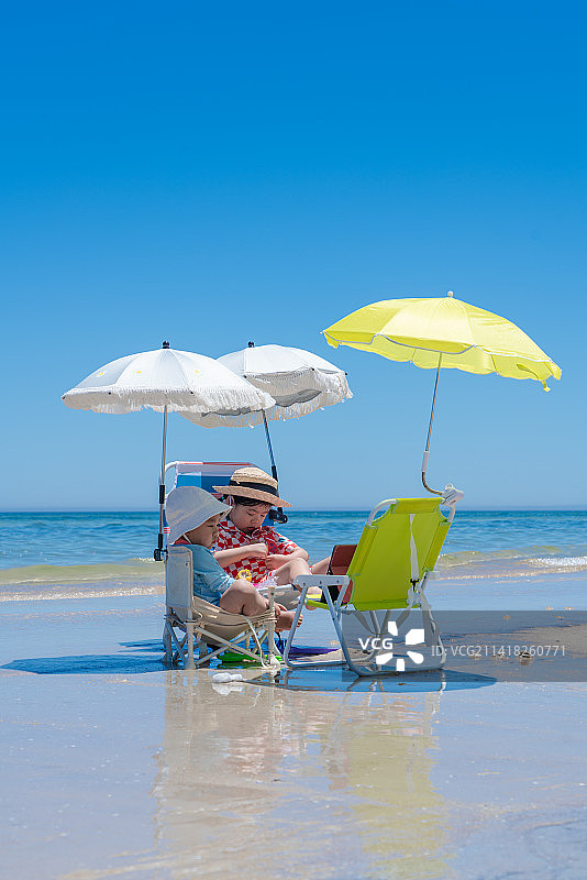 坐在海滩遮阳伞沙滩椅享受的两个小孩图片素材