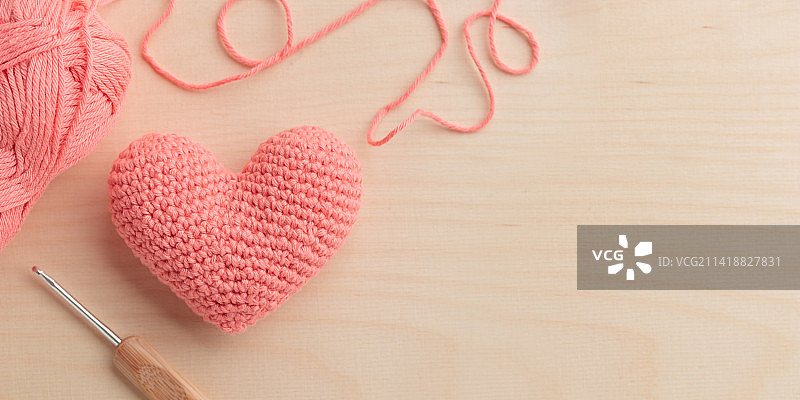 钩针编织的粉色爱心玩偶，搭配钩针和毛线，木质背景，情人节，芬兰图片素材