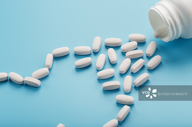 白色胶囊中的维生素和矿物质从蓝色背景的白色罐子中掉落，罗马尼亚图片素材