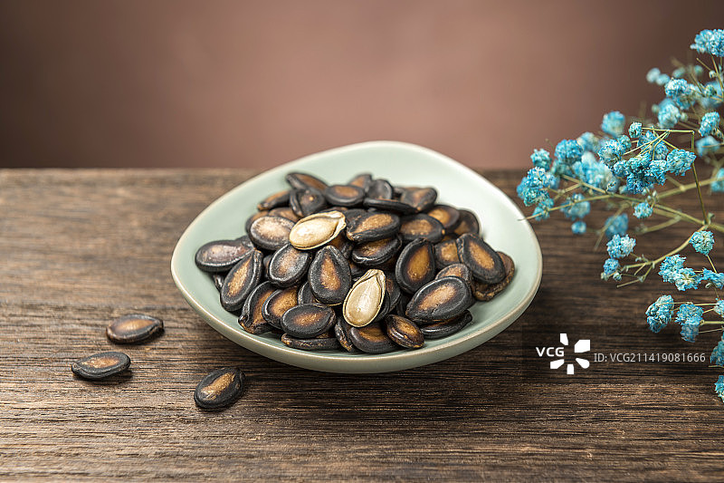 一盘西瓜子与茶水摆放在木桌面上特写图片素材