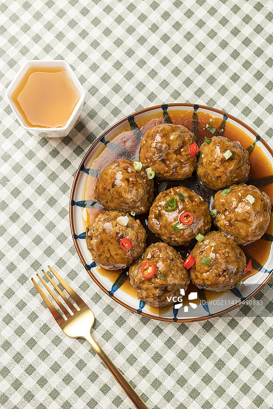 一盘红烧丸子摆放在格子桌布上特写蓝色背景图片素材