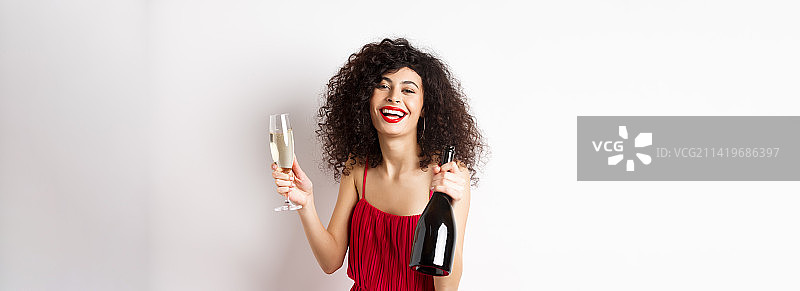 快乐的派对女人穿着红色连衣裙，笑着拿着酒瓶图片素材