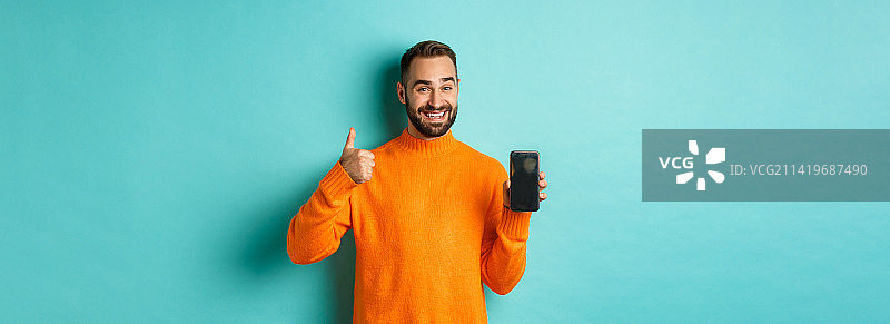 有吸引力的络腮胡男人展示智能手机屏幕，竖起大拇指图片素材