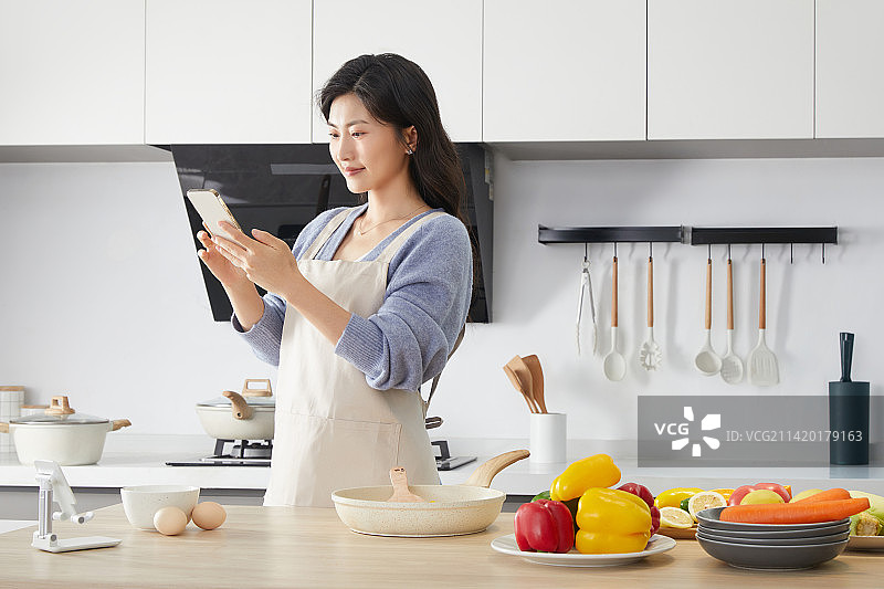 手拿手机围着围裙的年轻女人图片素材