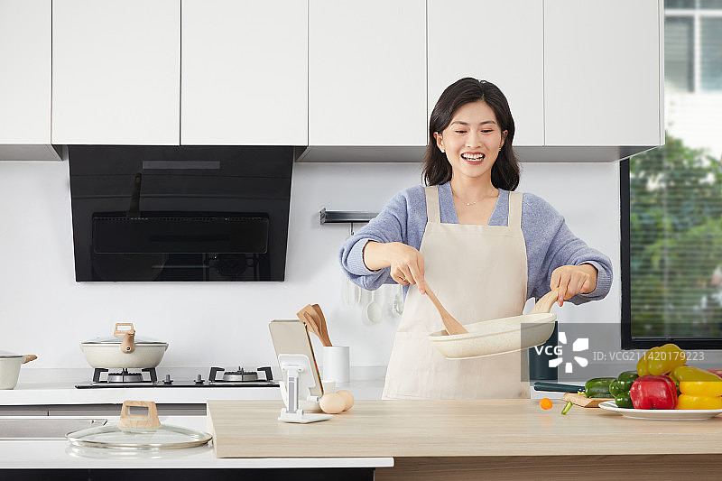 手拿锅铲的年轻女人在厨房忙碌图片素材