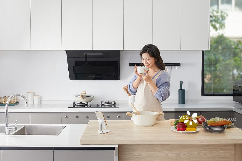 在厨房使用喝汤的年轻女人图片素材