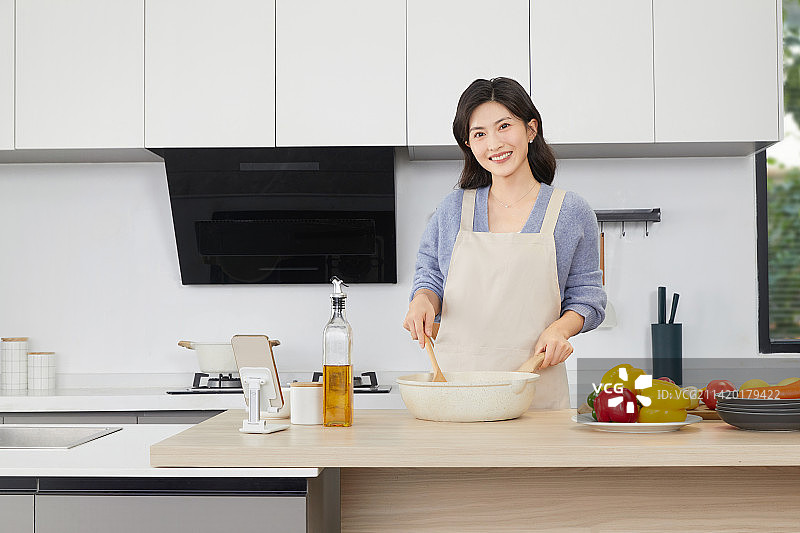 手拿锅铲的年轻女人在厨房忙碌图片素材