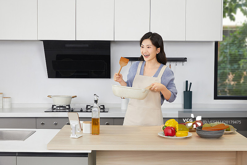 手拿锅铲的年轻女人在厨房忙碌图片素材