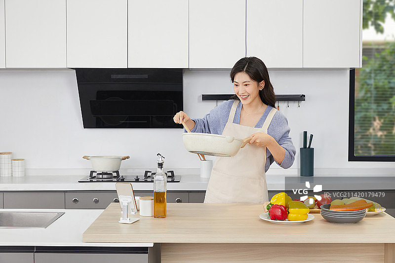 手拿锅铲的年轻女人在厨房忙碌图片素材