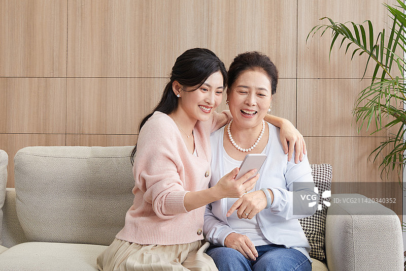 坐在客厅沙发分享手机的母女图片素材