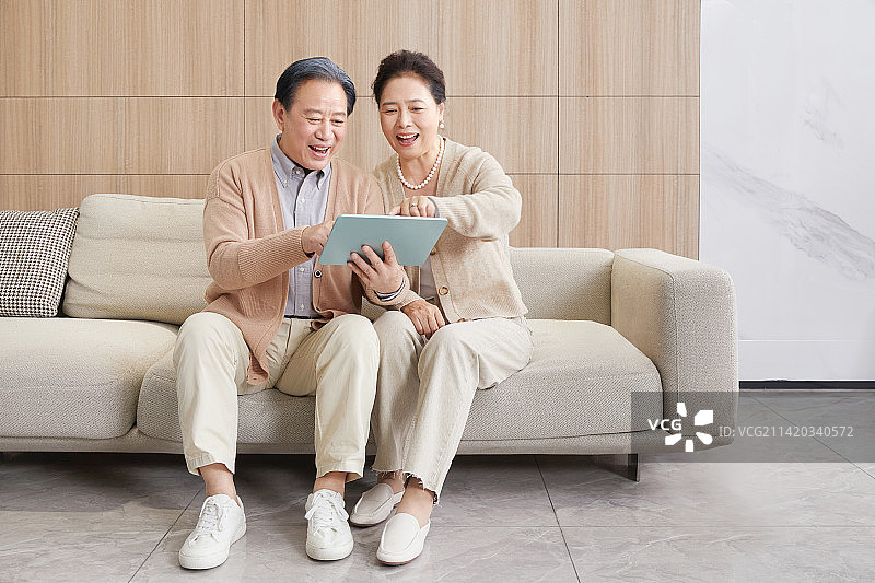 坐在客厅沙发玩手机与平板电脑的老年夫妻图片素材