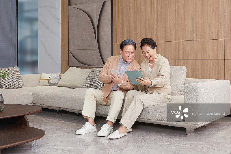 坐在客厅沙发玩手机与平板电脑的老年夫妻图片素材