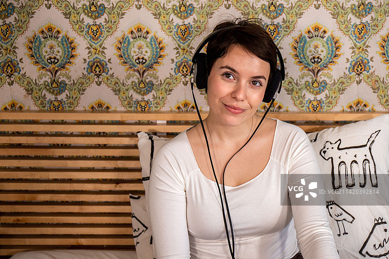 美女在床上戴着耳机听音乐，意大利图片素材