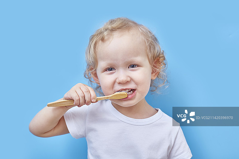 卷发女孩用木制牙刷在蓝色背景上刷牙图片素材