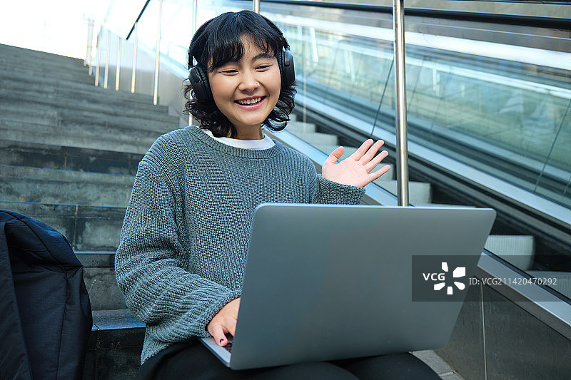 微笑的年轻学生戴着耳机坐在街边的台阶上图片素材