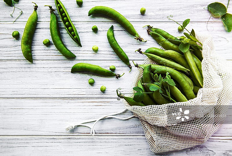 可重复使用的环保袋，装满新鲜豌豆荚，白色木质背景，罗马尼亚图片素材