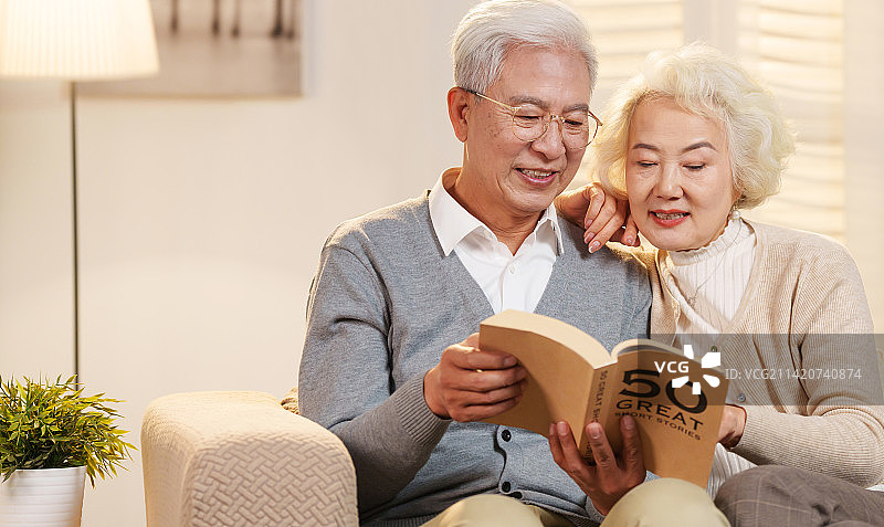 幸福的老年夫妇坐在沙发上看书图片素材