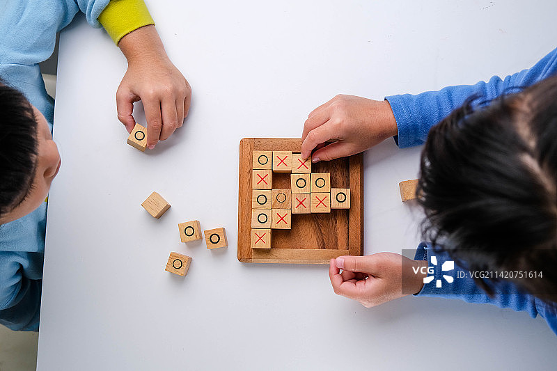 在客厅的桌子上玩井字棋木板游戏的小兄妹（泰国）图片素材