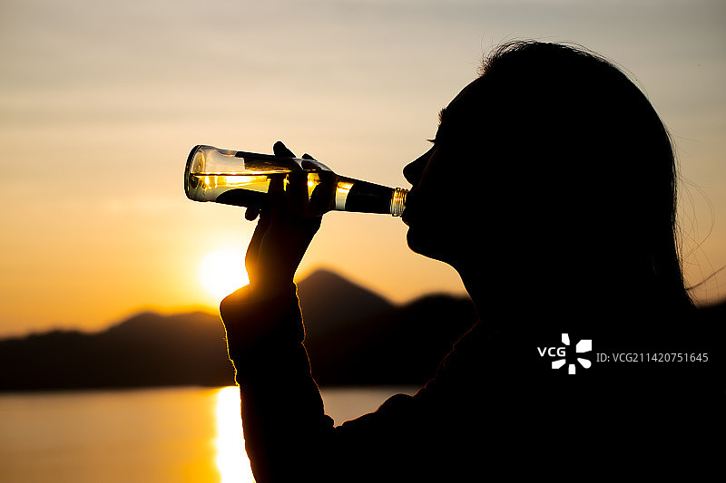 黄昏时分在泰国海滩喝水的女子轮廓剪影图片素材