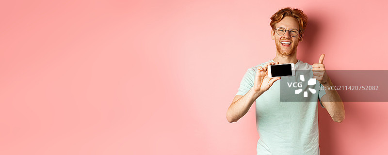 快乐的欧洲男人，姜黄色头发，戴着眼镜，展示手机空白屏幕图片素材