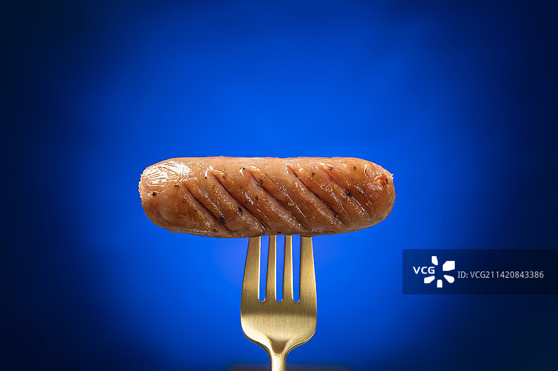 金色叉子叉香肠特写蓝色背景图片素材