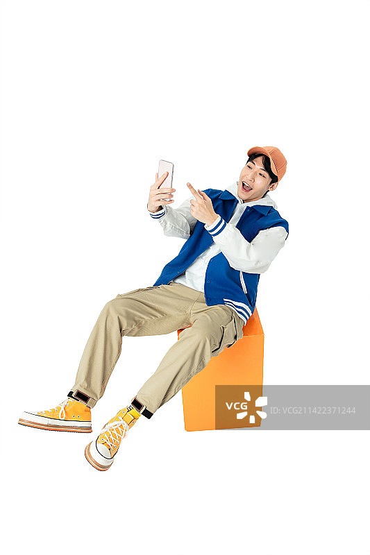坐在橙色凳木箱子上玩手机的年轻男生图片素材