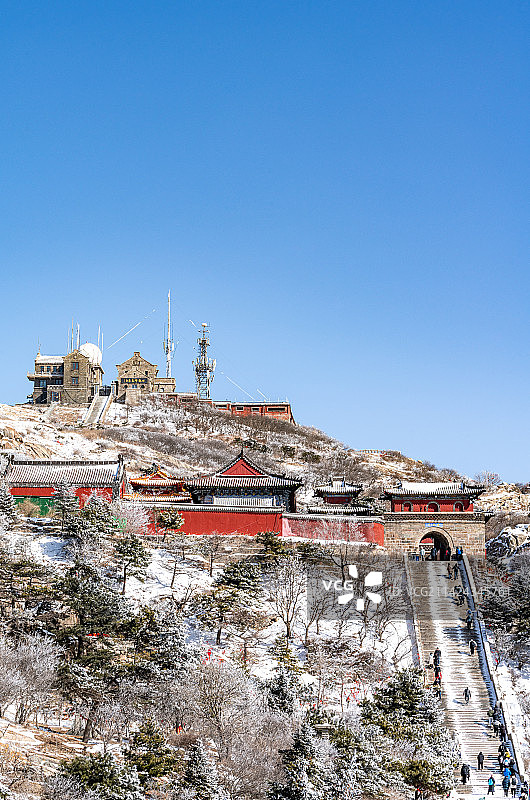 纯净蓝天白雪背景下的中国山东泰安泰山风景区碧霞祠西神门日观峰气象台建筑景观与登山的游客图片素材
