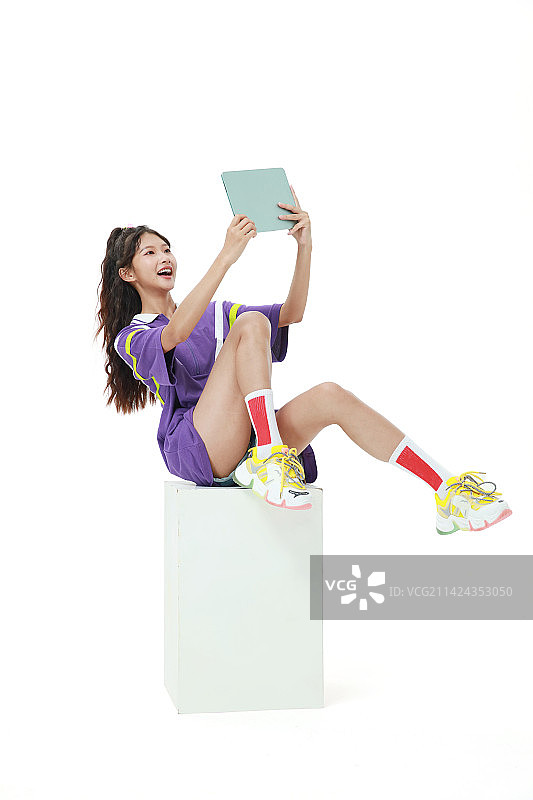 坐在木箱上玩平板电脑的美少女图片素材
