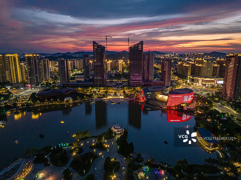 航拍溧阳燕湖公园平静的水面倒影着多彩的晚霞和城市的灯光，溧阳文化艺术中心玉兰花瓣建筑倒影在水中图片素材