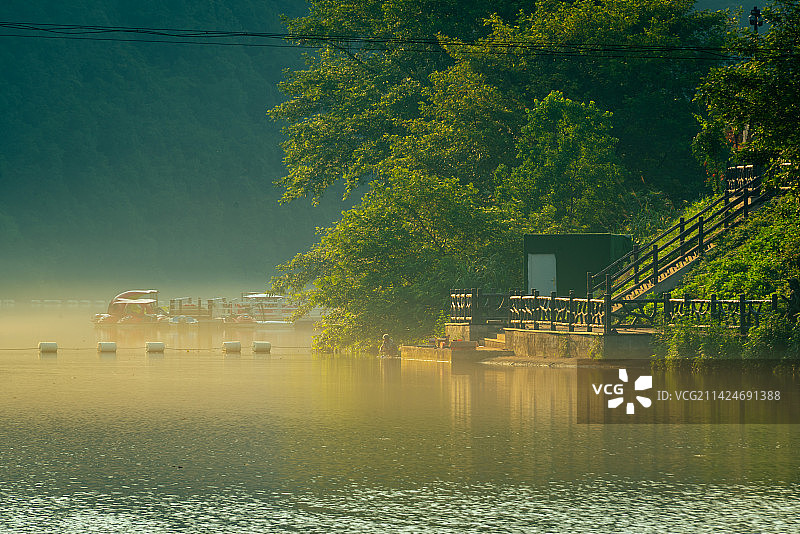 日出时分的皖南川藏线储家滩水库，水面平静如镜，倒影着郁郁葱葱的绿树，雾气被阳光照成金色图片素材