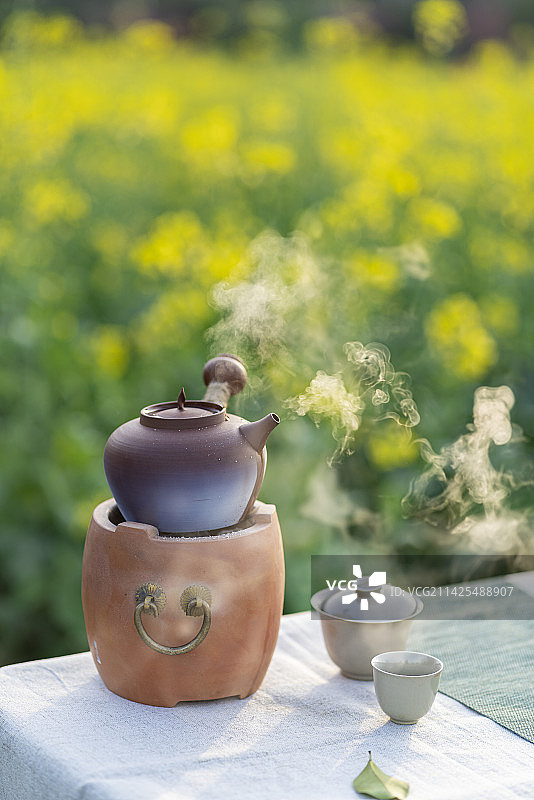 油菜花田边围炉煮茶的茶具与水果篮图片素材