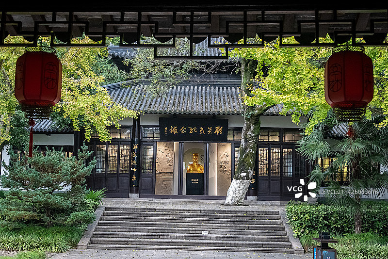 昆山亭林园顾炎武纪念馆建筑细节，透过前景的屋檐和灯笼，看见纪念馆的建筑和金色的顾炎武半身雕像图片素材