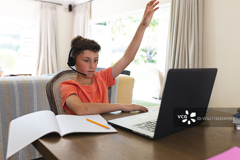 白人男孩坐在客厅里学习和使用笔记本电脑和耳机图片素材