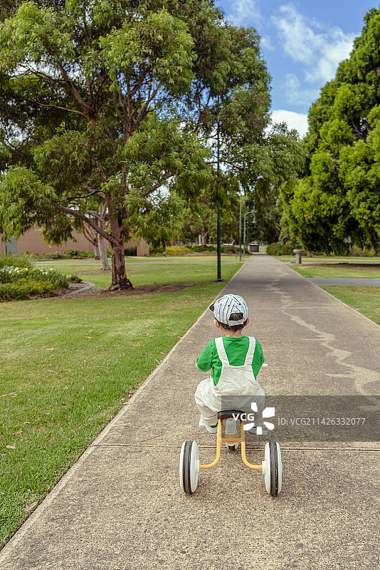 树林林荫小道上骑童车的棒球帽男孩图片素材