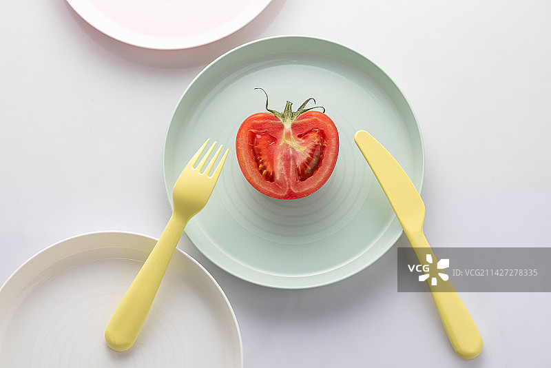 白色的桌面上，摆放着糖果色餐盘和餐叉餐刀，和切开的新鲜番茄西红柿图片素材