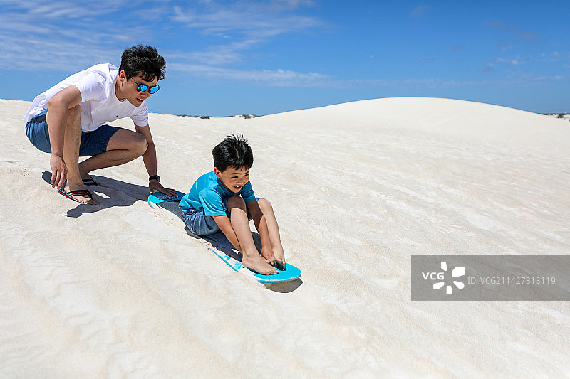 在白沙漠上玩滑板的中国父子图片素材