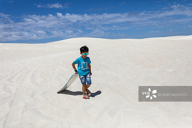 在白沙漠上玩滑板的中国小男孩图片素材