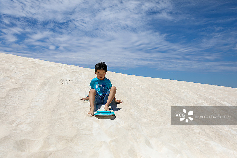在白沙漠上玩滑板的中国小男孩图片素材