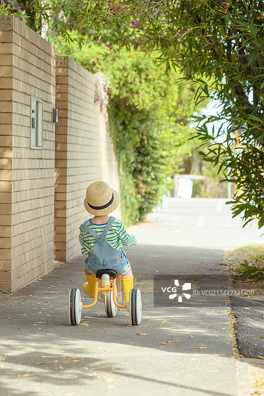 林荫小道上骑三轮童车的草帽男孩图片素材