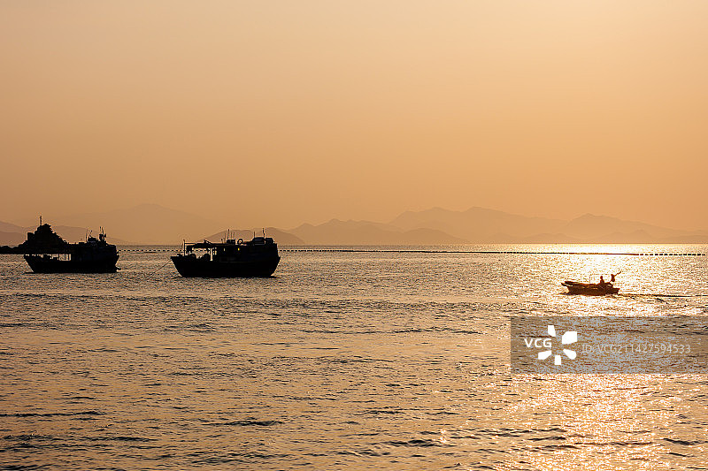 深圳南澳月亮湾日落停泊在海湾中的渔船与行驶中的快艇图片素材