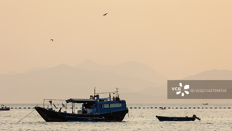 深圳南澳月亮湾日落停泊在海湾中的渔船与行驶中的快艇图片素材