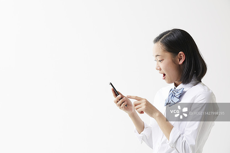 惊讶的高中女生看着她们的智能手机。图片素材